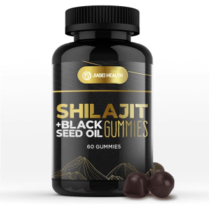 A black bottle of JiaBei Health Shilajit + Black Seed Oil Gummies with a gold label, featuring the product name prominently. Two dark-colored gummies are in the foreground, alongside raw black seed oil and a blue flower, visually representing the key ingredients. The label indicates "60 GUMMIES."