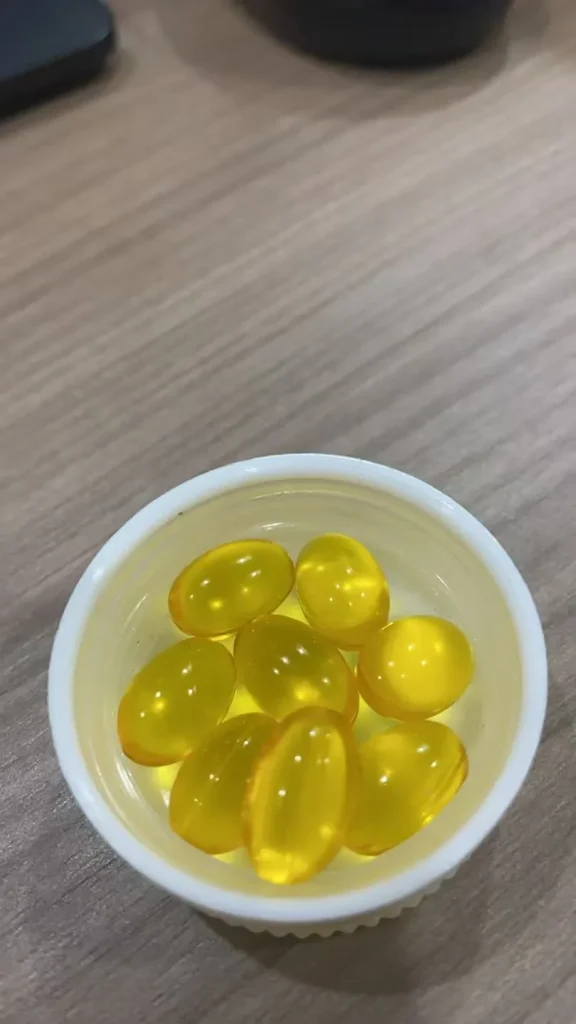 DHA softgel capsule samples in a white cup, transparent golden omega-3 supplement oil